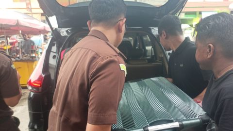 Petugas Kejati Sulut terlihat mengangkat koper hitam yang dijadikan barang bukti saat penggerebekan di sebuah toko emas di Kotamobagu, Senin (2/3/2026).
