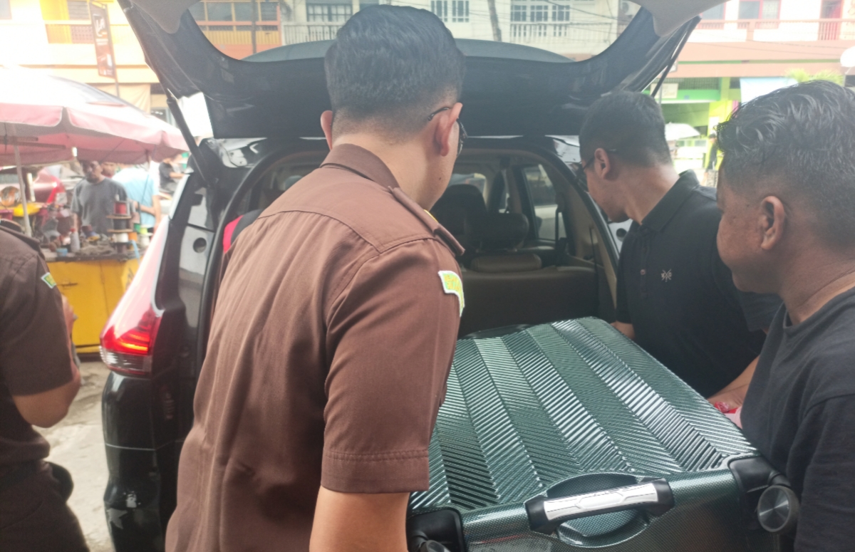 Petugas Kejati Sulut terlihat mengangkat koper hitam yang dijadikan barang bukti saat penggerebekan di sebuah toko emas di Kotamobagu, Senin (2/3/2026).