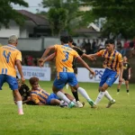 Aksi pemain Persibom saat berebut bola dengan tim lawan dalam laga Liga 4 Sulut. Pertandingan berlangsung sengit di lapangan hijau dengan dukungan penonton dari pinggir lapangan. Spanduk bertuliskan “Say No to Racism” turut menghiasi arena, menegaskan semangat sportivitas dan persatuan di tengah rivalitas kompetisi.