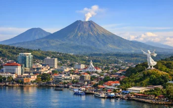 Harmoni di Nyiur Melambai: Pemandangan Kota Manado dengan latar Gunung Lokon yang ikonik. Keberhasilan Sulawesi Utara menembus 5 besar Indeks Kebahagiaan Nasional 2026 membuktikan bahwa keseimbangan antara pembangunan infrastruktur dan kualitas hidup masyarakat menjadi kunci kesuksesan di bawah kepemimpinan Gubernur Yulius Selvanus. (Foto: Dok. Istimewa)
