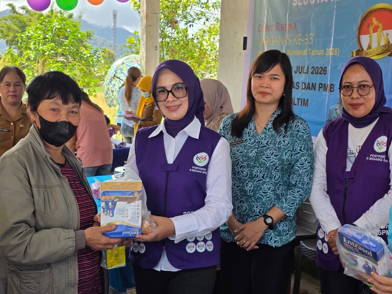 PULIH DAN SEHAT: Ketua TP Posyandu Kabupaten Boltim, Ny. Rosita Manoppo Pobela (tengah, rompi ungu), menyerahkan bantuan pemenuhan gizi secara simbolis kepada salah satu warga lansia saat memantau langsung pelaksanaan pelayanan Posyandu terintegrasi di Desa Bongkudai Baru. Kegiatan ini dirangkaikan dengan Pelayanan KB Serentak Sejuta Akseptor dalam rangka menyambut Hari Keluarga Nasional (Harganas) ke-33. Sumber: Facebook @Rosita Pobela