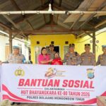 Sambut Hari Bhayangkara ke-80, Kapolres Boltim AKBP Golfried Hasiholan Pakpahan, S.H., M.Si. (ketiga dari kanan) bersama Ketua Bhayangkari Cabang Boltim Ny. Joice Golfried (keempat dari kanan) menyerahkan bantuan sosial berupa kemeja kepada seorang warga lansia (penerima manfaat) di Kecamatan Tutuyan. Penyerahan simbolis ini dilakukan di depan spanduk acara saat aparat kepolisian menyambangi warga secara door-to-door sebagai bentuk nyata kepedulian di tengah guyuran hujan.