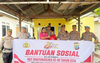 Sambut Hari Bhayangkara ke-80, Kapolres Boltim AKBP Golfried Hasiholan Pakpahan, S.H., M.Si. (ketiga dari kanan) bersama Ketua Bhayangkari Cabang Boltim Ny. Joice Golfried (keempat dari kanan) menyerahkan bantuan sosial berupa kemeja kepada seorang warga lansia (penerima manfaat) di Kecamatan Tutuyan. Penyerahan simbolis ini dilakukan di depan spanduk acara saat aparat kepolisian menyambangi warga secara door-to-door sebagai bentuk nyata kepedulian di tengah guyuran hujan.