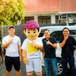 Ketua Askot PSSI Kotamobagu dengan kaos putih berdiri di samping maskot resmi Totabuan Champions League (TCL) 2026. Di sisi kanan, Wali Kota Kotamobagu dr. Weny Gaib mengenakan kaos hitam, bersama-sama menunjukkan dukungan atas peluncuran maskot “Bojo” yang akan memeriahkan turnamen di Stadion Nunuk Matali.