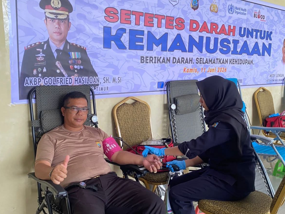 Kapolres Boltim AKBP Golfried Hasiholan Pakpahan mengacungkan jempol saat mendonorkan darahnya dalam acara peringatan Hari Bhayangkara ke-80. Kegiatan ini berlangsung di Aula Sanika Satyawada dengan latar belakang spanduk bertema "Setetes Darah untuk Kemanusiaan", Kamis (11/6/2026).