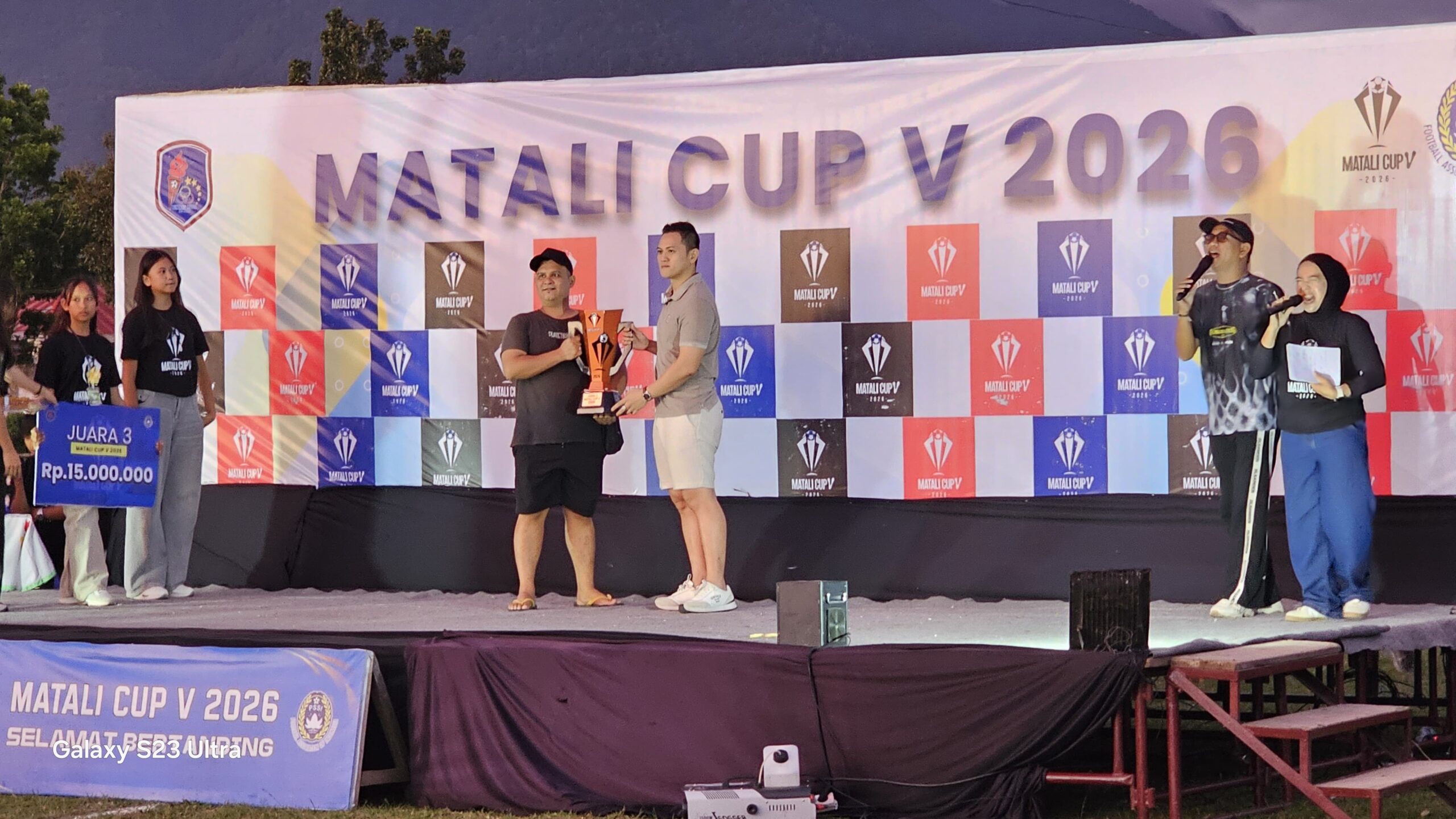 Ketua Askot PSSI Kotamobagu, Michael Solat Bibisa (berbaju putih), menyerahkan trofi juara Matali Cup V 2026 kepada Manajer PSM Mopusi di panggung utama Stadion Nunuk Matali. Penyerahan ini menandai berakhirnya turnamen bergengsi yang berlangsung sukses dan kondusif, sekaligus menjadi momentum menuju agenda besar berikutnya — Totabuan Champions League. Foto: Sulutplus/Bang Pace