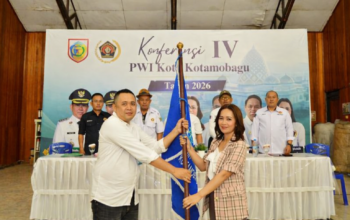 Ketua PWI Kotamobagu terpilih periode 2026–2029, Konni Balamba (kiri), menerima bendera organisasi dari perwakilan pengurus PWI Sulawesi Utara dalam Konferensi IV PWI Kota Kotamobagu di Gedung Kominfo, Jumat (26/6/2026).
