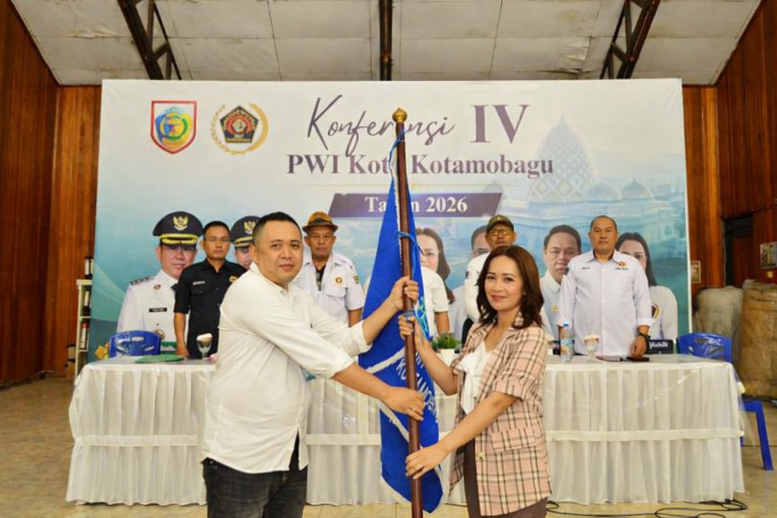 Ketua PWI Kotamobagu terpilih periode 2026–2029, Konni Balamba (kiri), menerima bendera organisasi dari perwakilan pengurus PWI Sulawesi Utara dalam Konferensi IV PWI Kota Kotamobagu di Gedung Kominfo, Jumat (26/6/2026).
