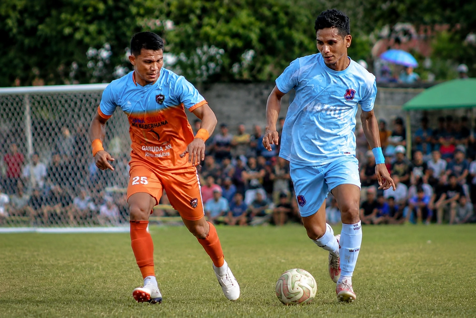 Pemain Bintang Muda Matali (jersey biru langit) mencoba menguasai bola di bawah pengawalan ketat pemain ZM FC Bolsel (jersey oranye) pada laga final Totabuan Champions League (TCL) 2026 di Lapangan Nunuk, Kotamobagu, Minggu (9/8/2026).